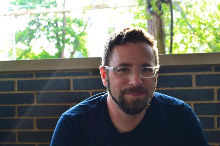 Associate Professor Seth Brodsky sitting in front of a brick wall and window