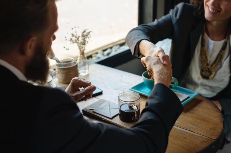 Stock image of a man and woman in business dress shaking hands at a table in a coffee shop