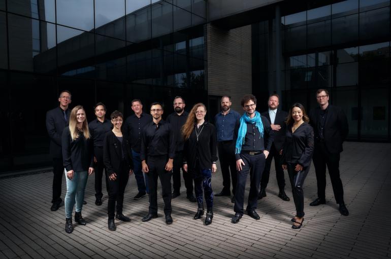 A larger group of people in black posing in front of a modern building.