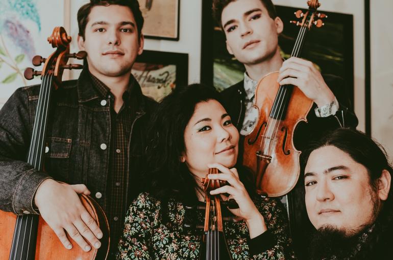 Four people pose with string instruments in hand