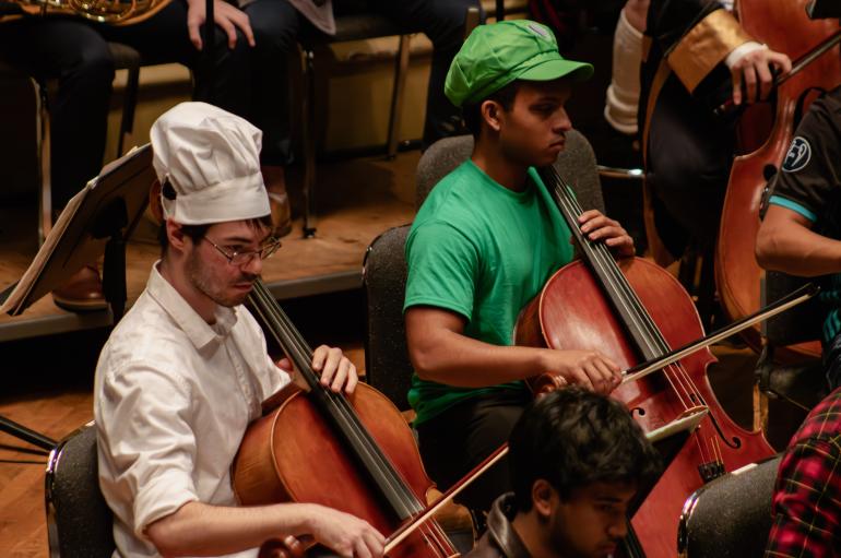 A cellist in a chef costume and a cellist in a Luigi costume perform on stage