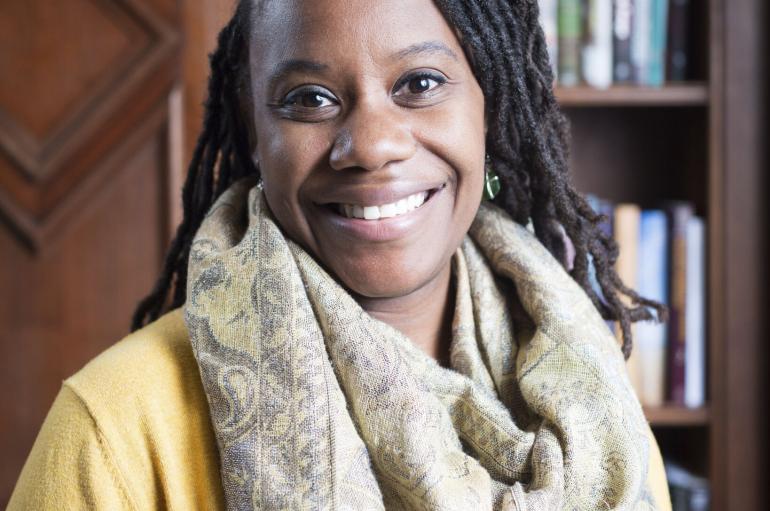 A woman in a yellow cardigan and white scarf smiles at the camera