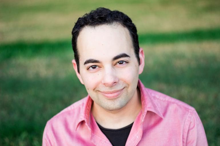 A headshot of a man in a pink shirt smiling at the camera