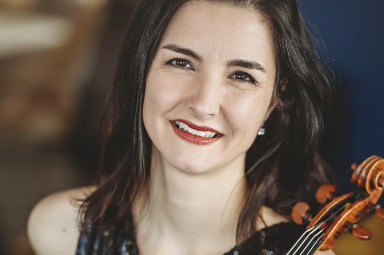 A headshot of a woman smiling and holding a viola