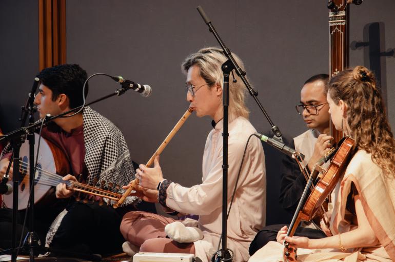 4 performers are seated playing traditional South Asian instruments