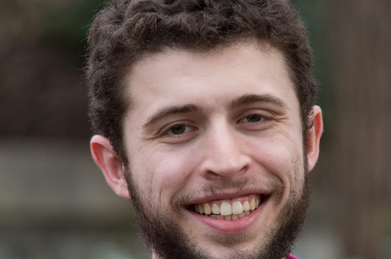Headshot of a man with dark brown hair and a beard smiling