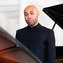 Aaron Diehl headshot between two open grand pianos
