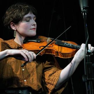 A person in a yellow shirt plays the viola with their eyes closed
