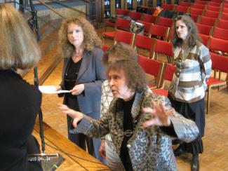 A woman gestures with her hands while speaking to musicians on a stage.