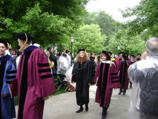 Two women in academic garb walk down the sidewalk at an outdoor convocation.