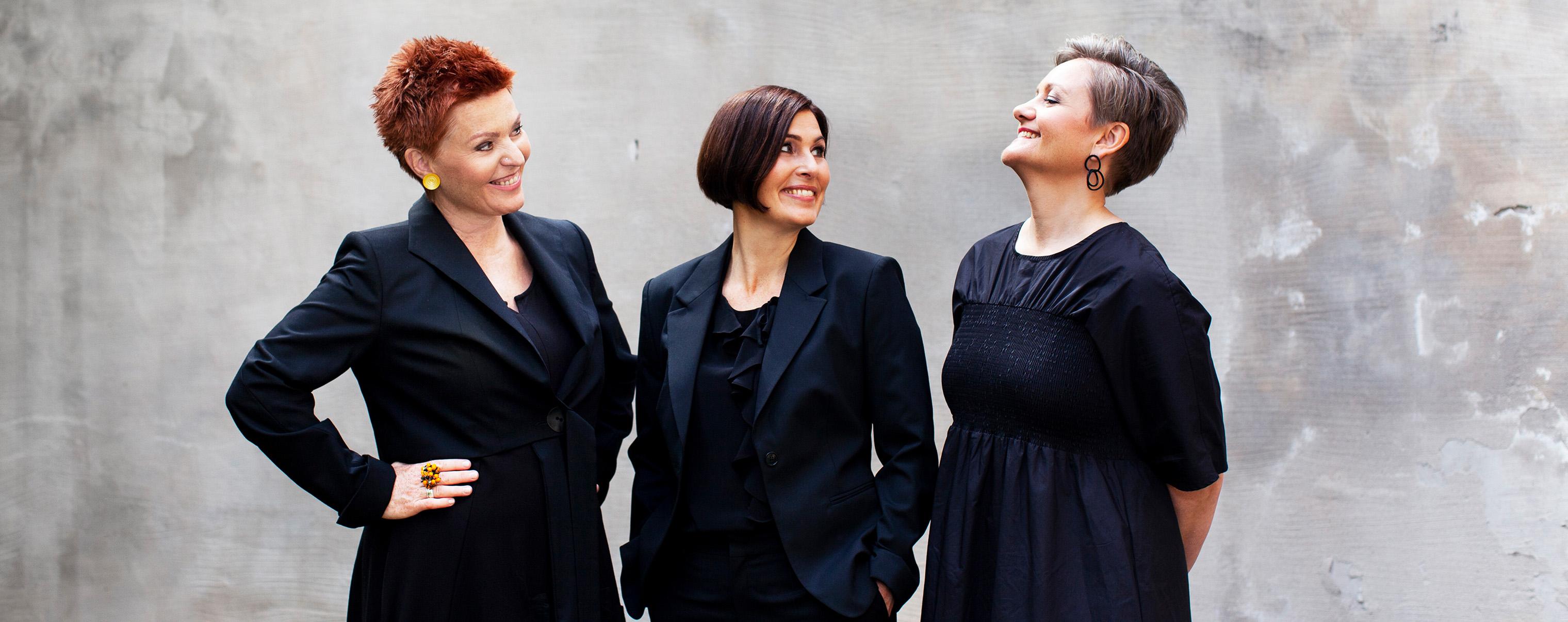 Trio Mediæval members standing against a gray wall