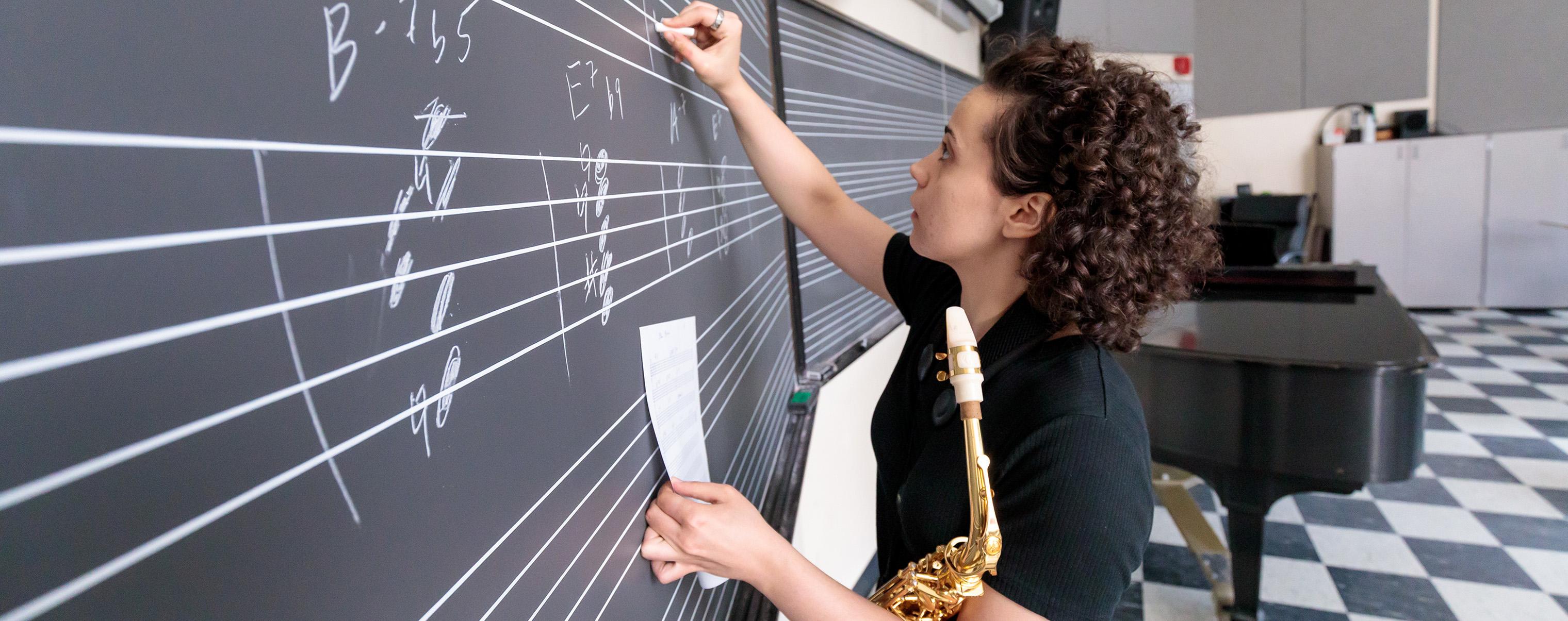 Student writing on chalkboard with saxophone in hand