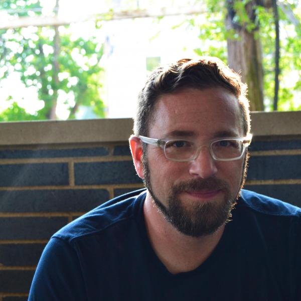 Associate Professor Seth Brodsky sitting in front of a brick wall and window