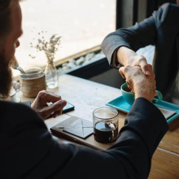 Stock image of a man and woman in business dress shaking hands at a table in a coffee shop