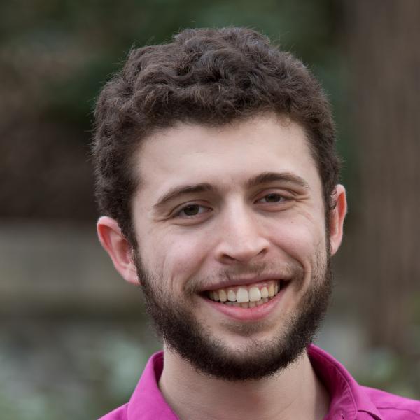 Headshot of a man with dark brown hair and a beard smiling